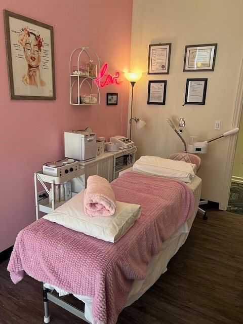 Cozy spa room with a pink theme, treatment bed, skincare equipment, and certificates on the wall.